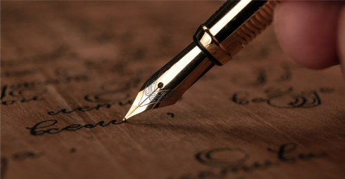 Fountain pen in the hand with paper with ink text on the wooden desk closeup. 
